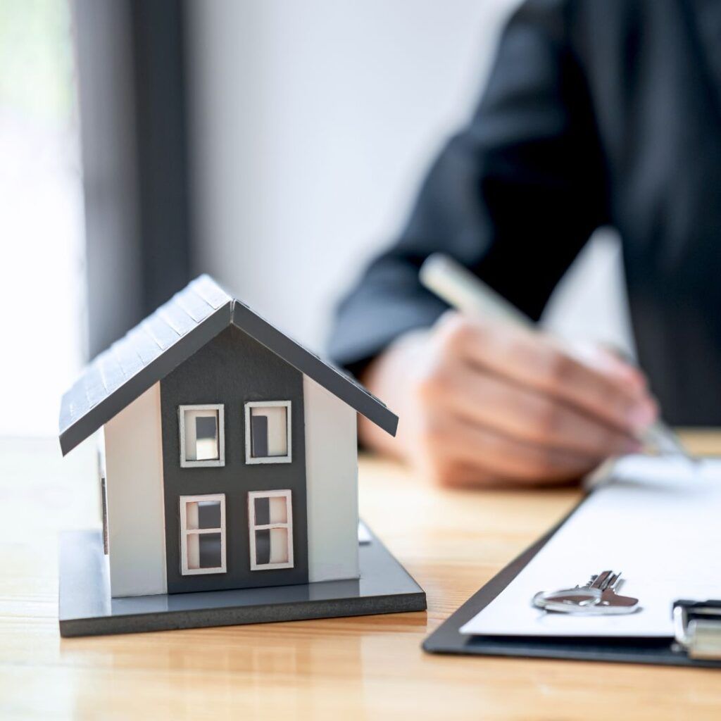 Miniature house next to paperwork and hand writing, possibly a real estate transaction.