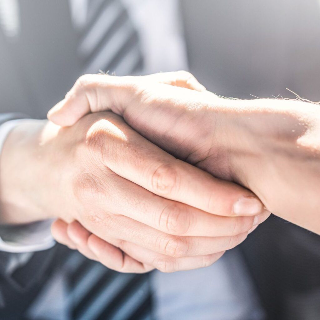 Two hands clasped in a handshake; business attire visible.