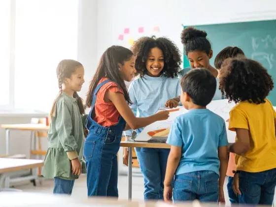 Children gathered around a table in a classroom, looking at papers.