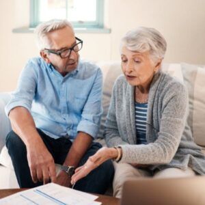Couple reviewing paperwork, woman gestures while man looks on, seated in a living room.