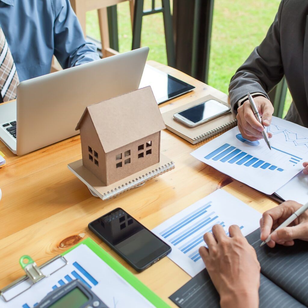 Real estate professionals reviewing financial data with a model house on a desk.