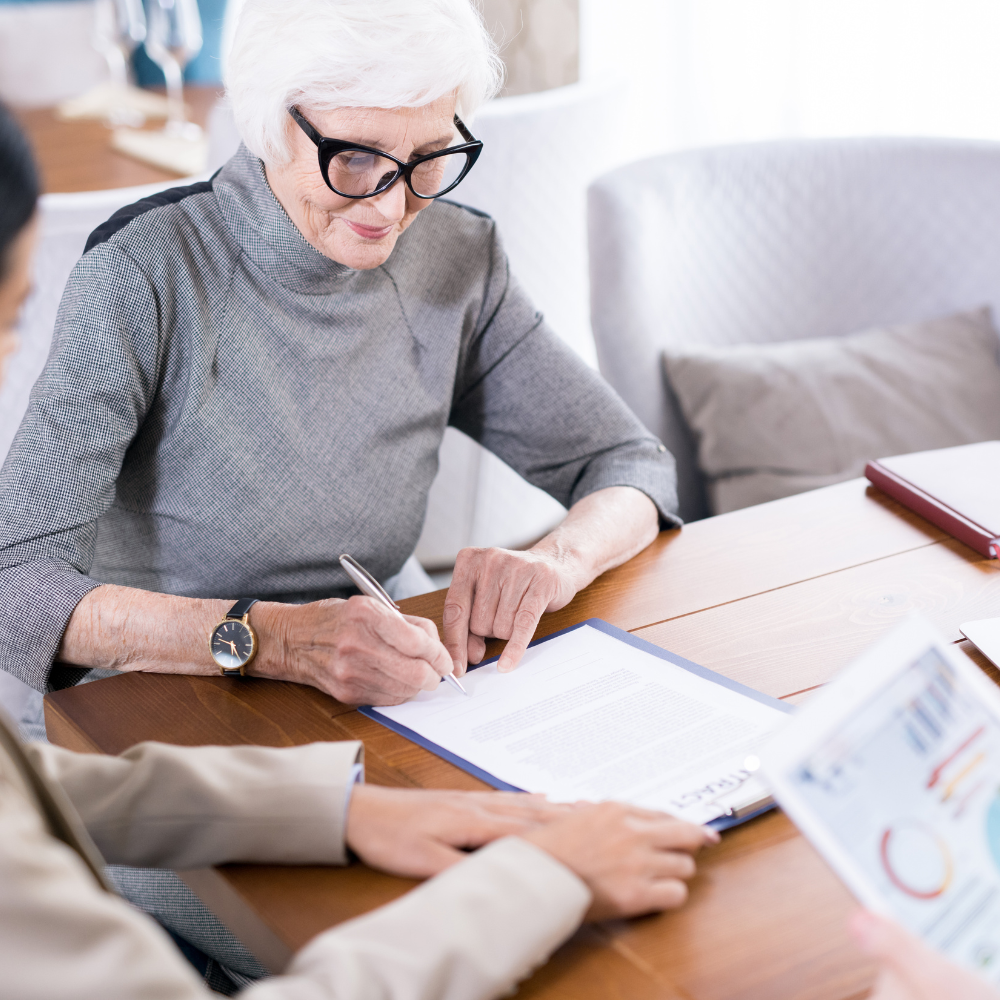 Woman signing a document at a table, with another person looking at papers.