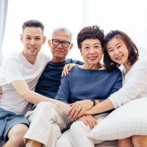 Family of four smiling, sitting on a couch. Two younger adults and two older adults, indoors.