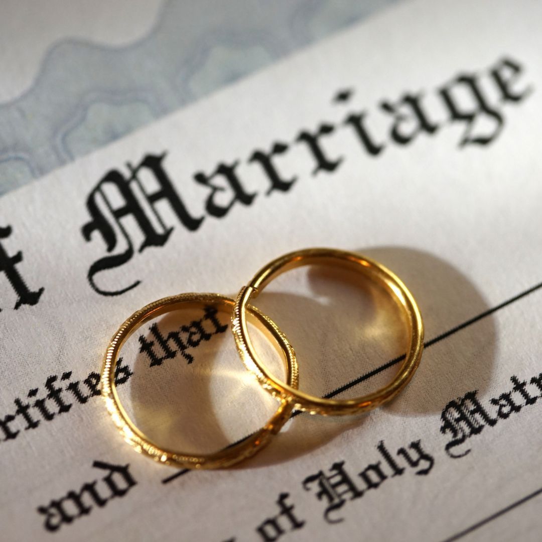 Two gold wedding rings on top of a marriage certificate.