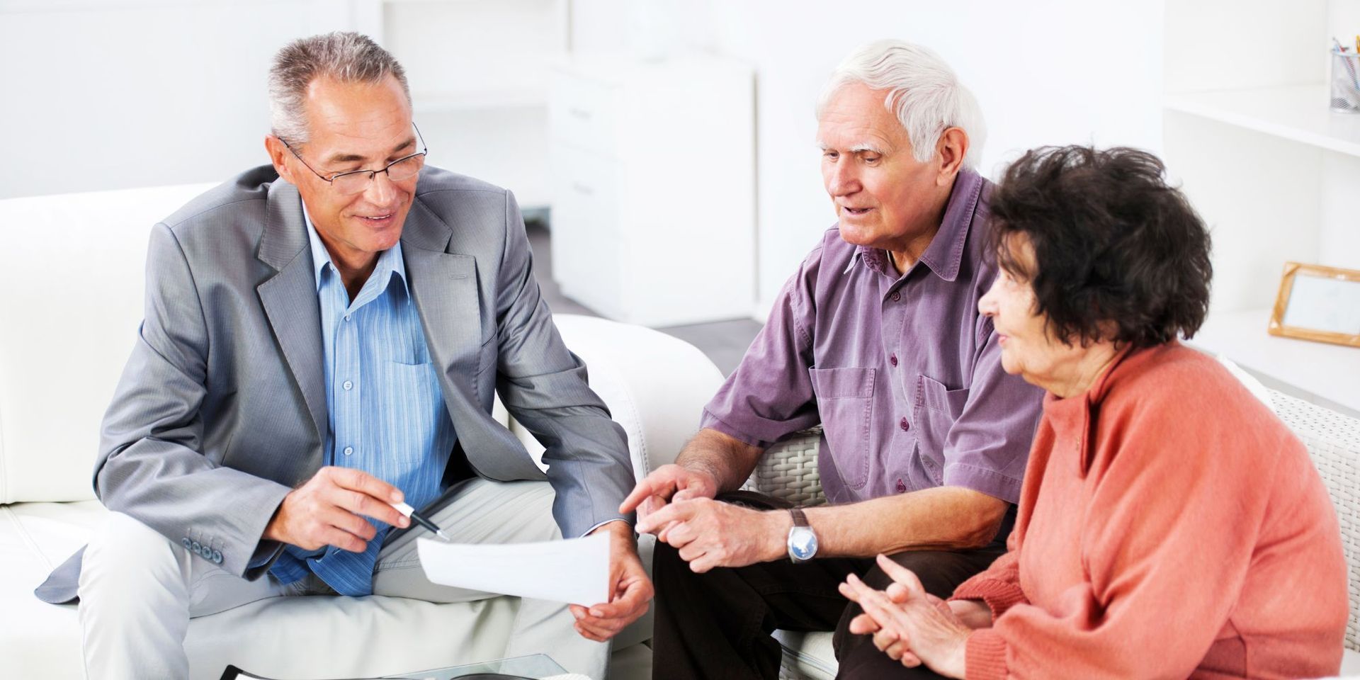 A man in a suit explaining paperwork to an elderly couple on a couch.