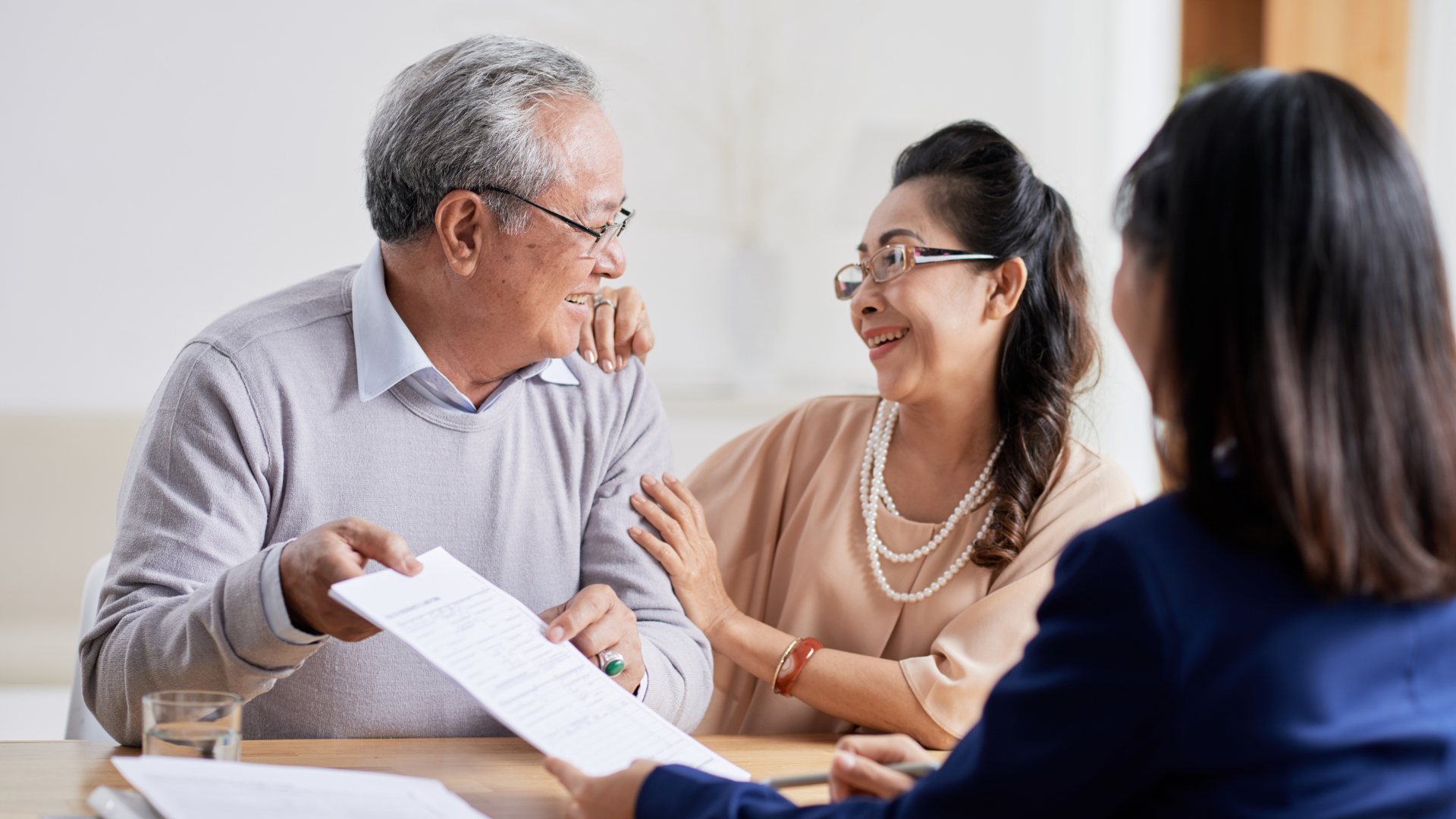 Older couple smiles at a person as they review paperwork at a table.
