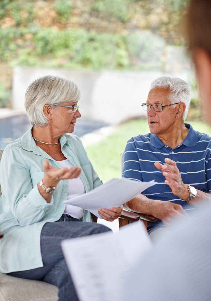 Couple reviewing documents, gesturing while seated outdoors, discussing.