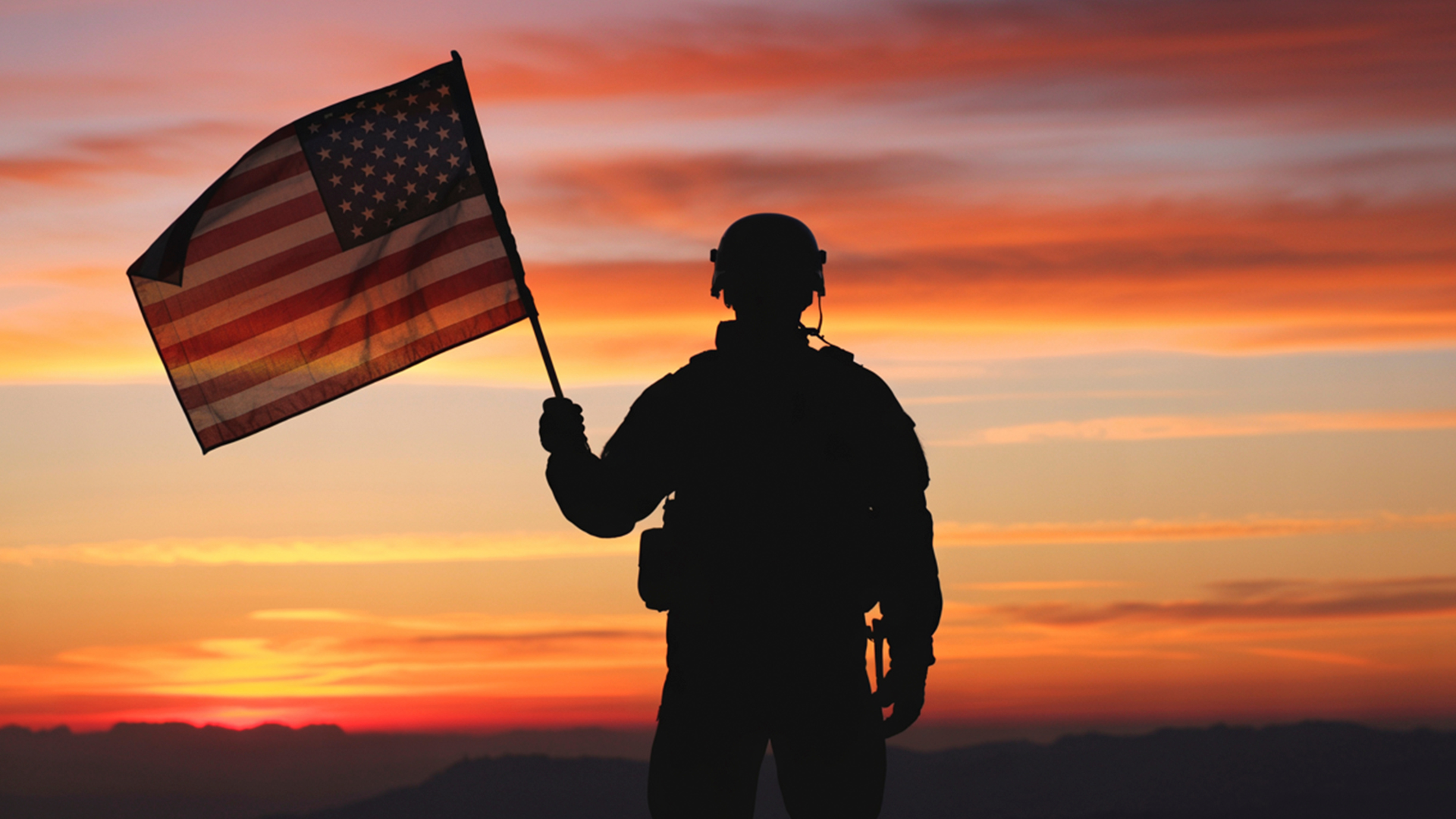 Silhouette of a soldier holding an American flag against a sunset.