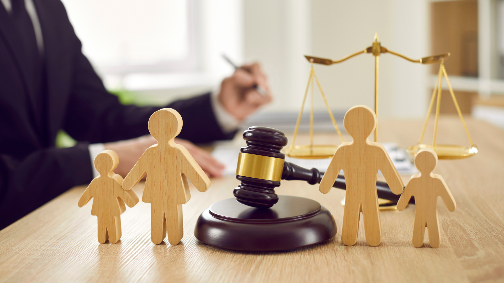 Lawyer with gavel and scales of justice; wooden family figures on desk.