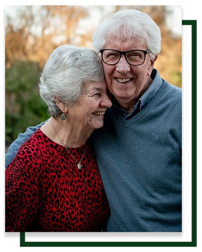 Smiling couple embracing outdoors. Woman in red top, man in blue sweater and glasses.