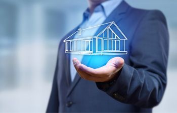 Man in a suit holding a glowing outline of a house in his hand, representing real estate.