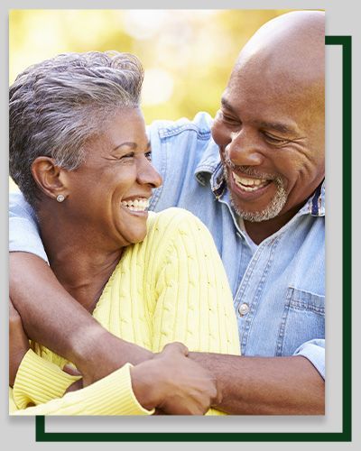 Smiling couple embracing outdoors. Woman in yellow, man in denim.