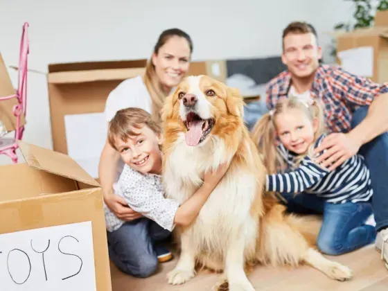 Family with two children and a dog surrounded by moving boxes, smiling.