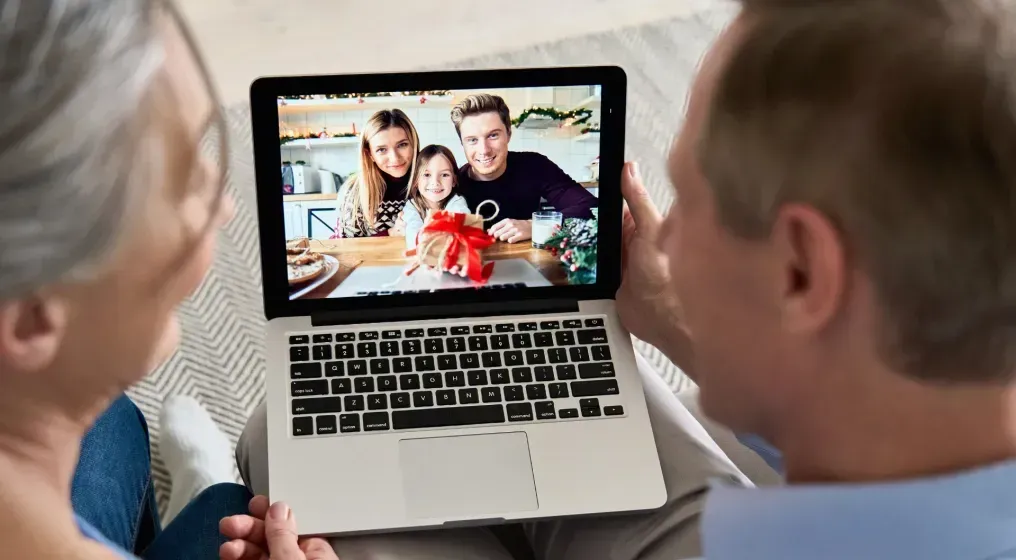 Two people on couch video-calling a family holding a gift.