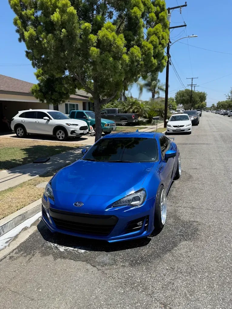 Blue sports car parked on a sunny residential street with houses and trees nearby