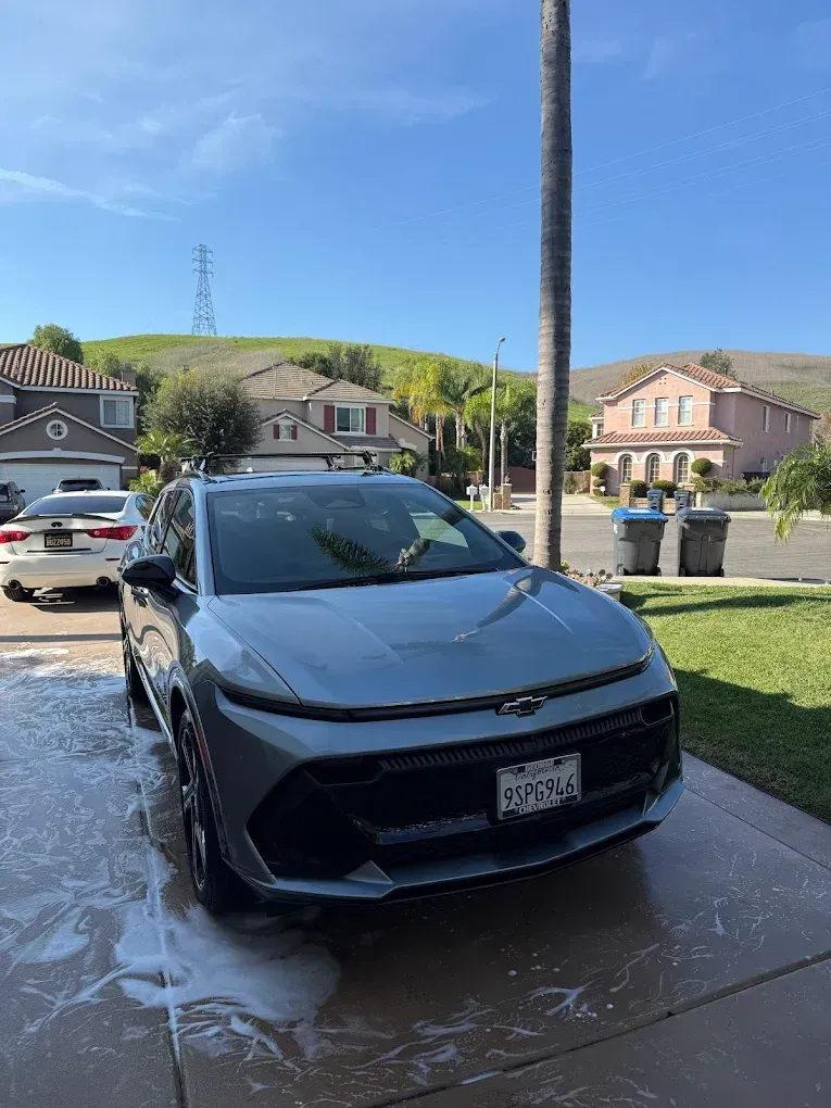 Black sedan parked on a wet driveway in a suburban neighborhood, with houses and hills in the background