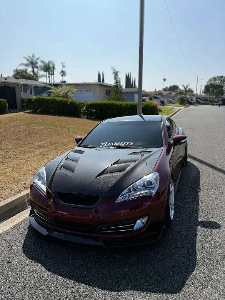 Maroon sports car parked on a sunny residential street with a windshield banner and hood vents