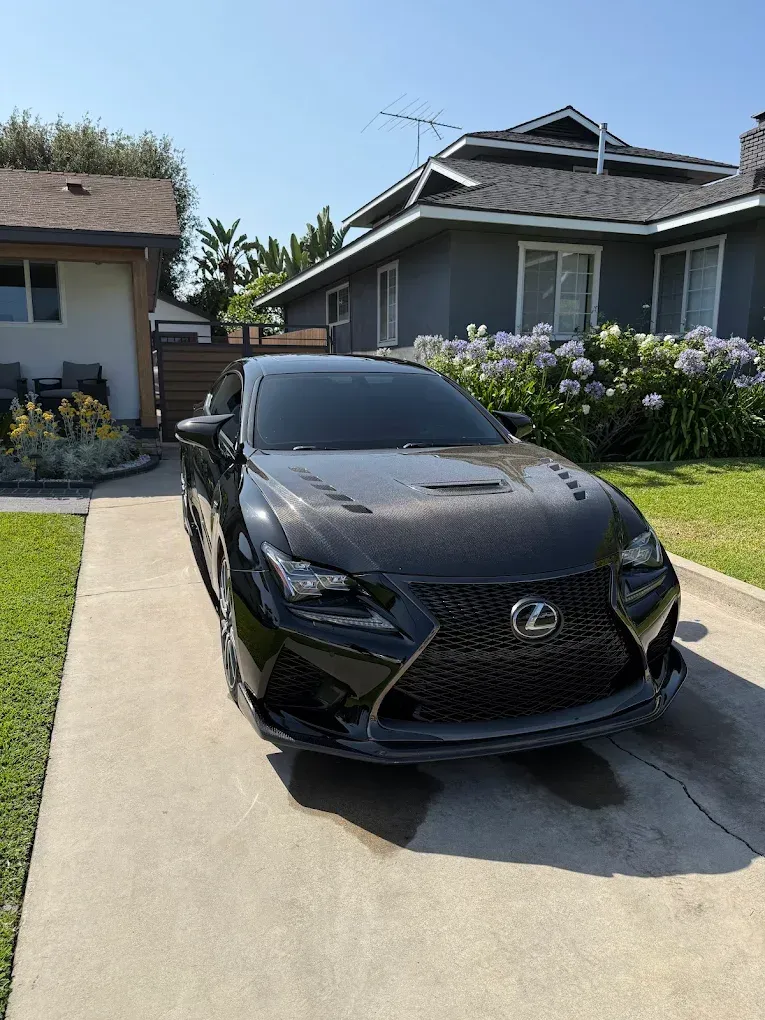 Black Lexus SUV parked in a driveway in front of a suburban house on a sunny day