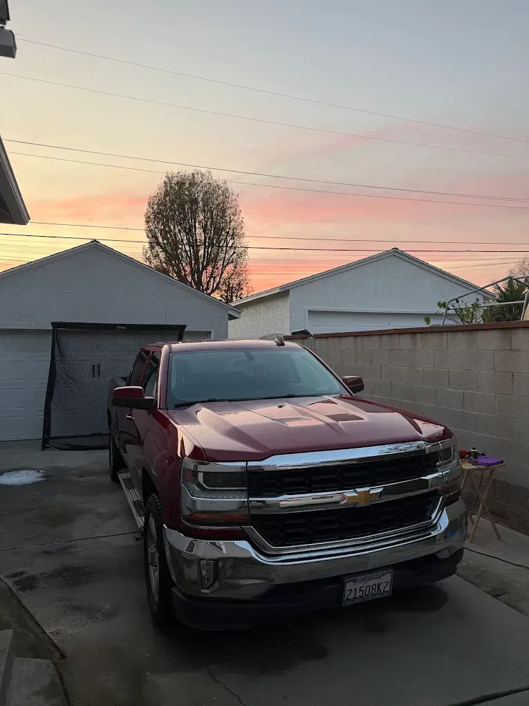 Red pickup truck parked in a driveway at sunset with garage and fence behind it