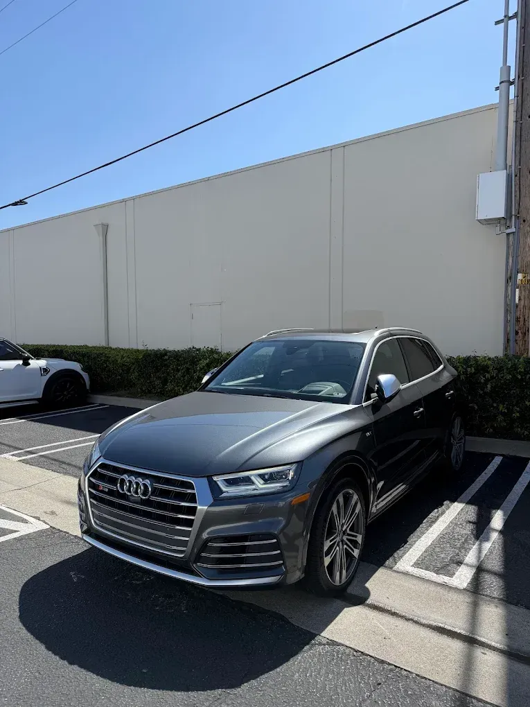 Dark gray Audi SUV parked in a sunny lot beside a beige building