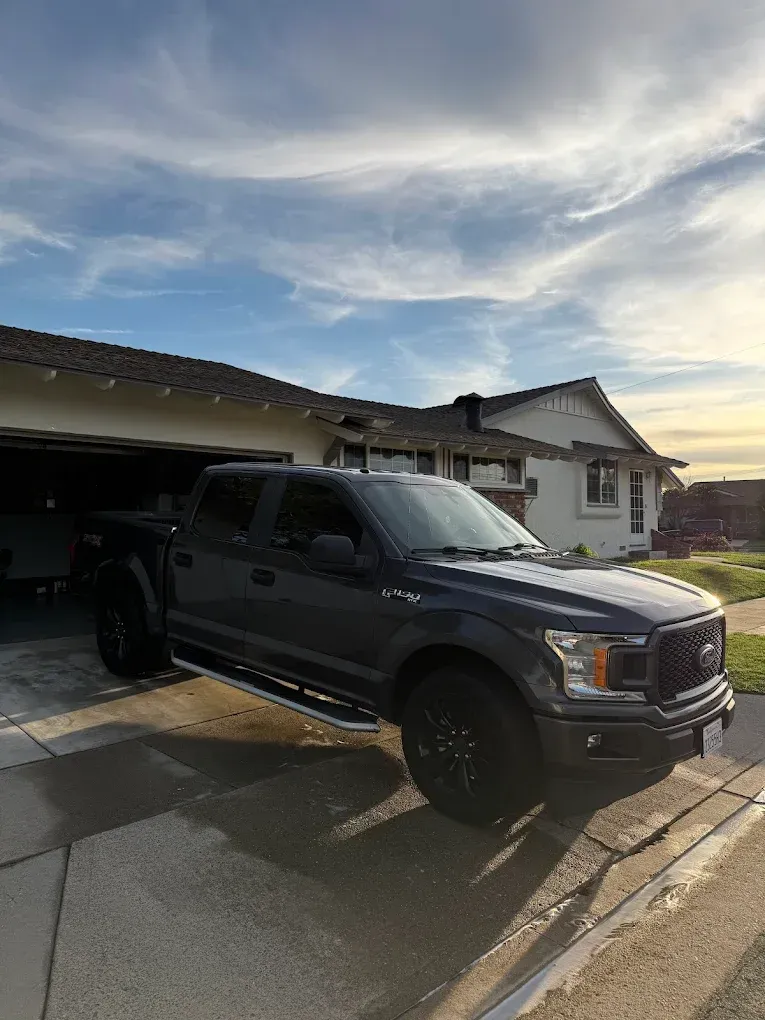 Black pickup truck parked in a wet driveway beside a suburban house at sunset