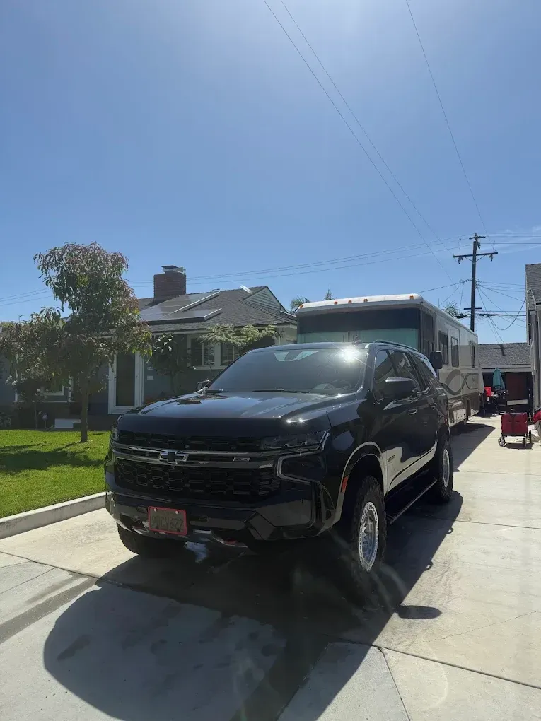 Black lifted pickup truck parked in a sunny residential driveway under a clear blue sky