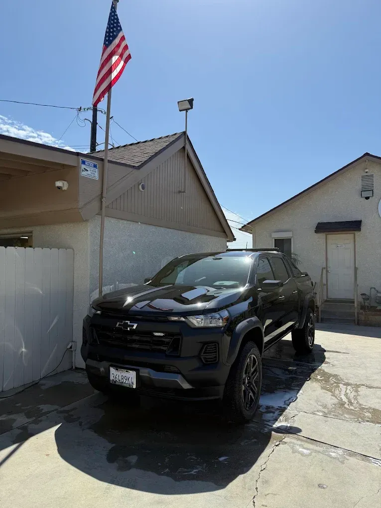 Black Ford pickup parked in a driveway beside a house, with an American flag overhead.