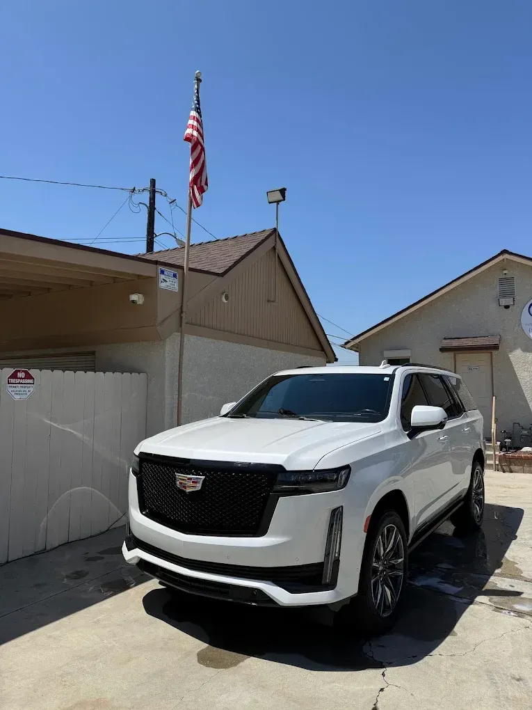 White Cadillac SUV parked in a driveway beside a house under a clear blue sky