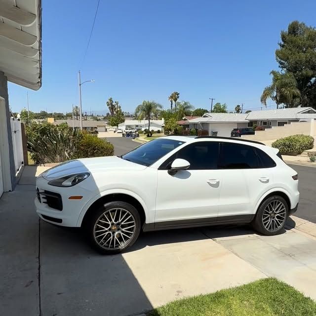White SUV parked in a driveway beside a house on a sunny day
