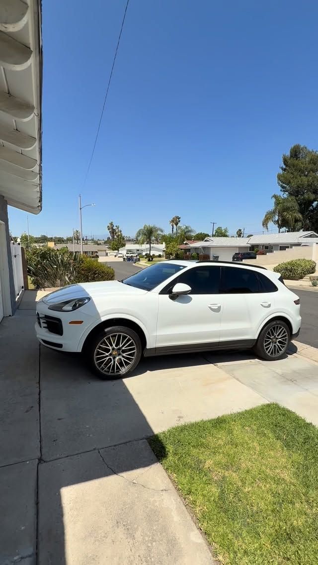 White SUV parked in a driveway beside a house under a clear blue sky.