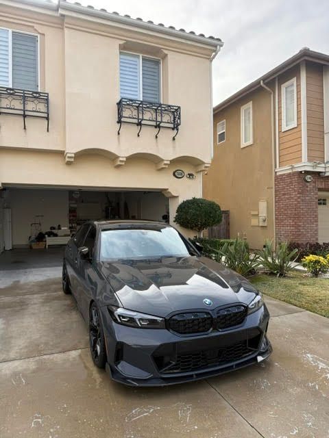 Black BMW parked in a driveway outside a two-story tan townhouse and open garage