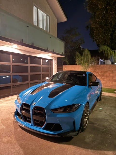 Blue sports sedan parked in a driveway at night outside a garage, front view.