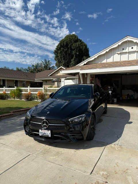 Black Mercedes sedan parked in a driveway beside a suburban house under a blue sky