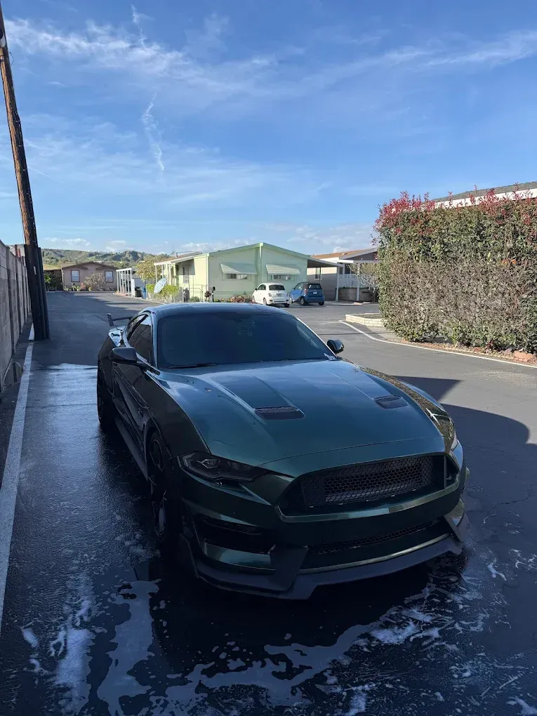 Green sports car parked on a wet street beside a building, under a blue sky.