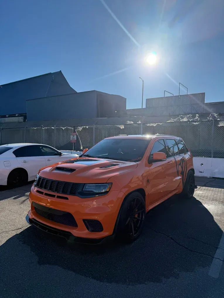 Orange SUV parked outdoors in bright sun beside a white car and building.