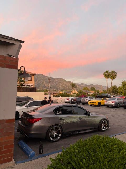 Parking lot at sunset with a dark gray car, mountains in the distance, and pink clouds overhead