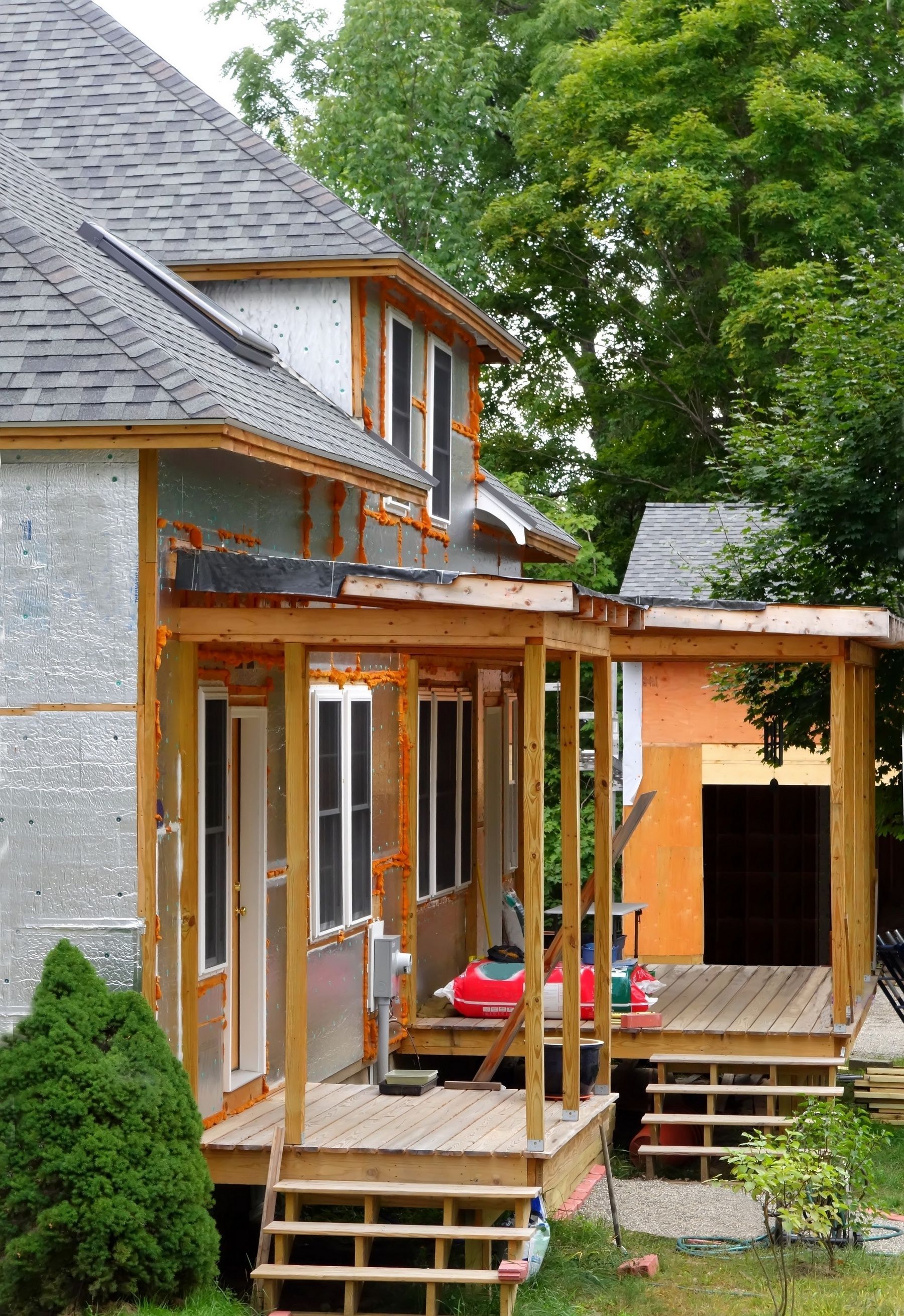 House under construction with porch and stairs; gray siding and brown wood framing.