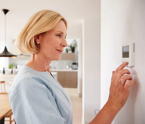 Close Up Of Mature Woman Adjusting Central Heating Temperature At Home On Thermostat