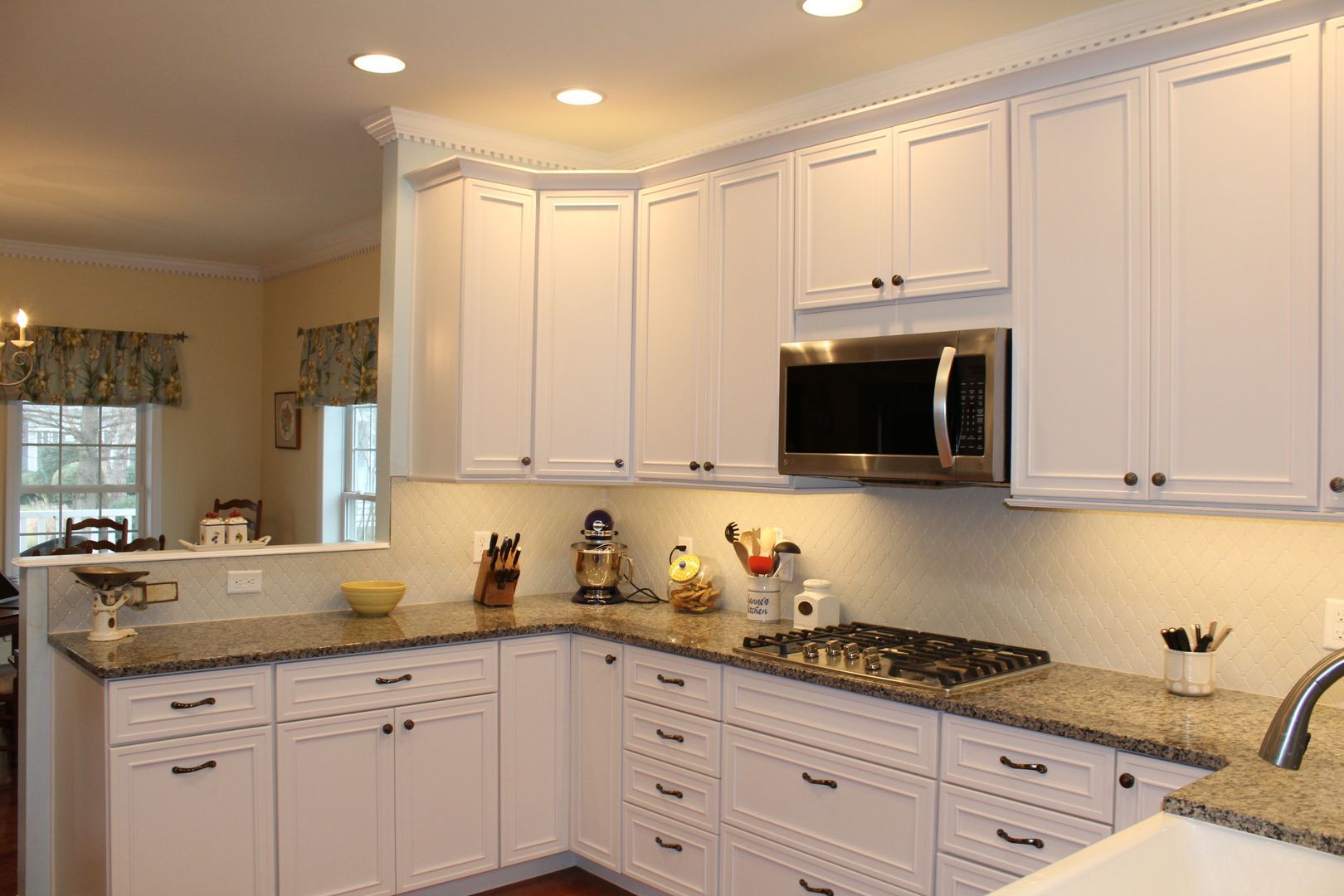 A kitchen with white cabinets , granite counter tops , a stove and a microwave.
