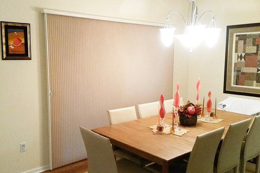 A dining room featuring a wooden table, chairs, a chandelier, wall art, and light-colored vertical blinds on a patio door.