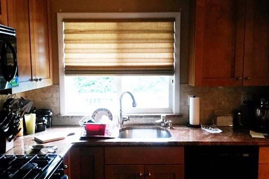 Kitchen sink area with a window, bamboo shade, granite countertops, and wooden cabinetry.