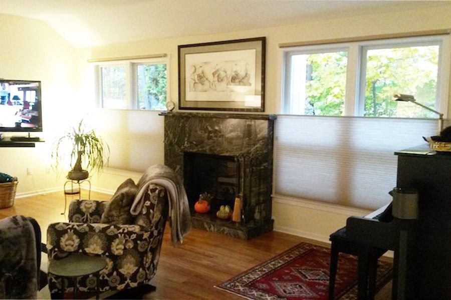 A living room featuring a patterned armchair, a dark marble fireplace, a piano, and a television.