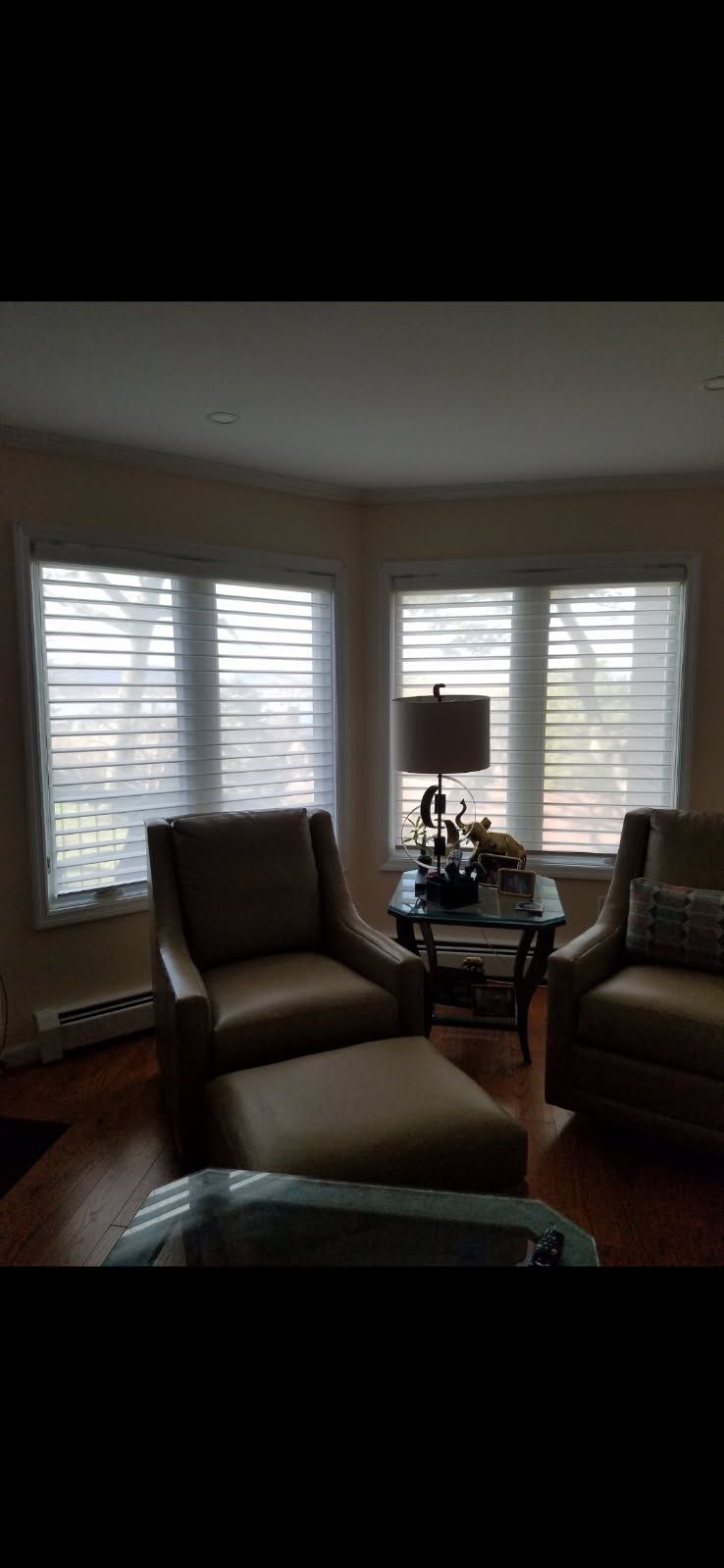 Two armchairs with a matching ottoman, separated by a small table with a lamp, positioned near two corner windows.