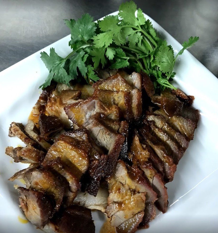 Sliced, glazed barbecued pork on a white plate, garnished with cilantro.