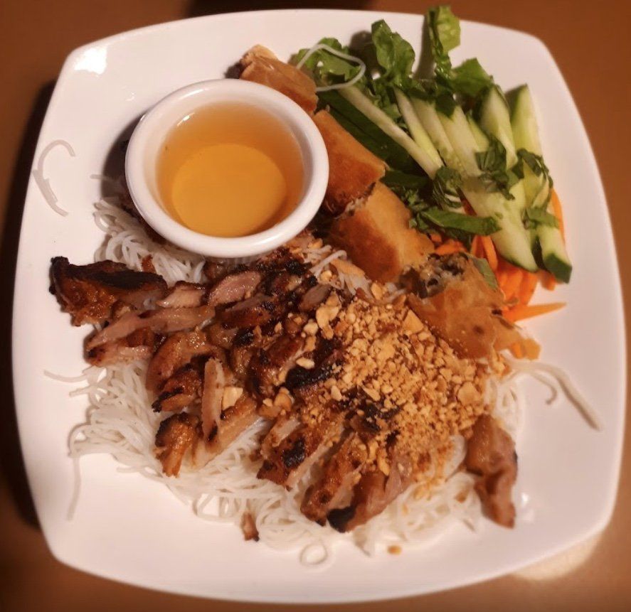 Bún chả dish: grilled pork, vermicelli noodles, vegetables, fried spring rolls, peanuts, and dipping sauce.