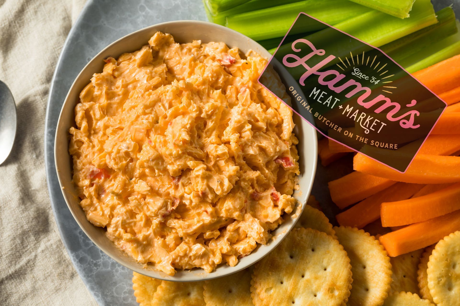 A bowl of dip with crackers and carrots on a plate.