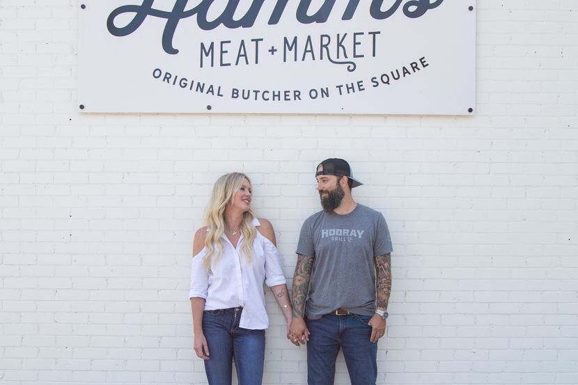 A man and a woman are holding hands in front of a meat market sign.