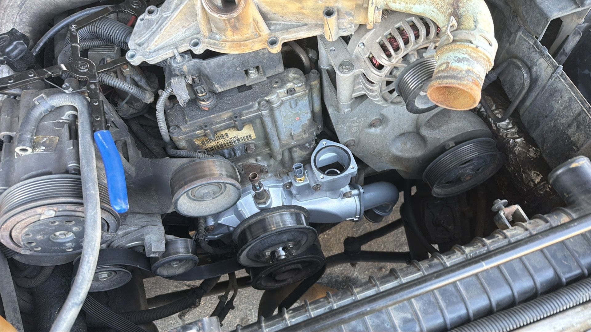 Open car engine bay with belts, pulleys, and hoses exposed, viewed from above