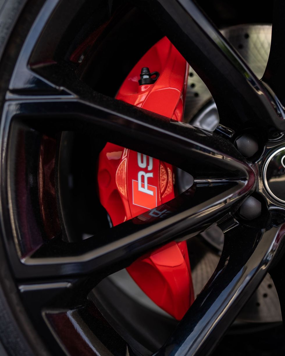 Black car wheel with a red brake caliper visible behind the spokes.