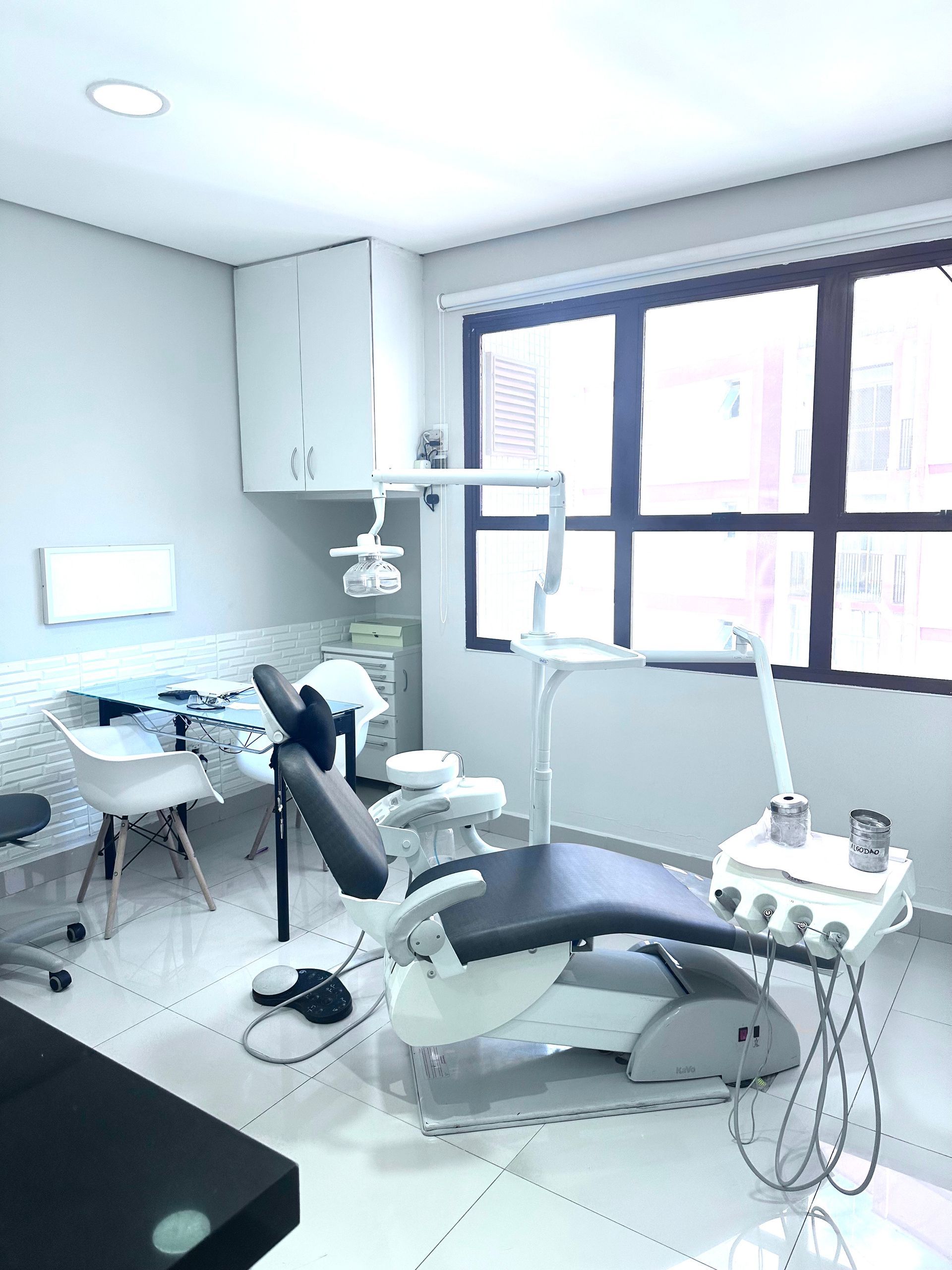 Consultório odontológico com cadeira odontológica, equipamentos e janela.